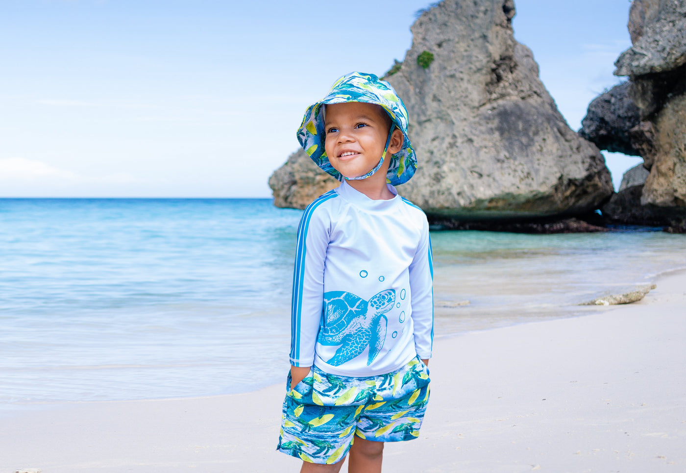 boy wearing salty turtle hat, rashguard and swim trunks on the beach