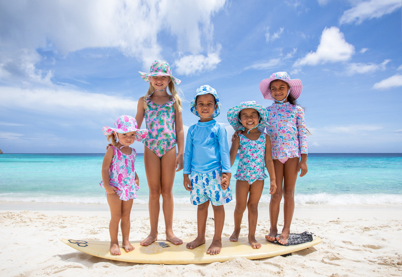kids on the beach wearing flap happy hats and swimwear standing on the surf board at the beach