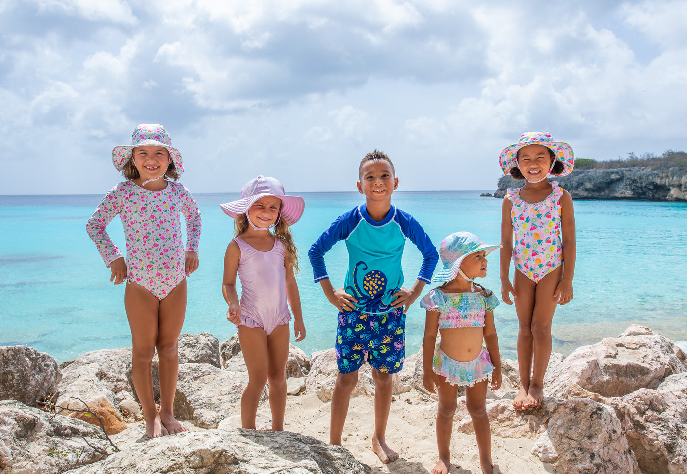 Children posing for an image wearing flap happy at the beach. Swimwear is all from the spring/summer 2023 collection.