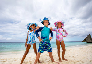 two happy grils and a happy boy wearing flap happy swimwear and hats posing on the beach