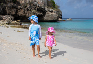 Girl and Boy walking on the beach wearing matching Flap Happy Swimwear in blue and pink seahorses