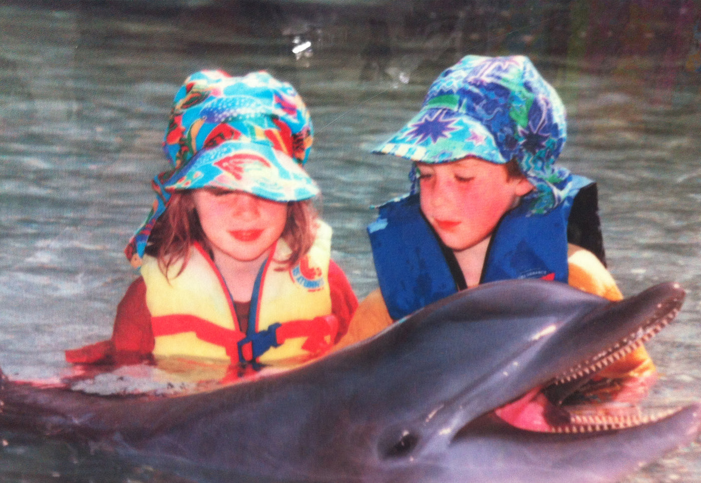 Kelly and cody in the water with a dolphin wearing Flap Happy hats